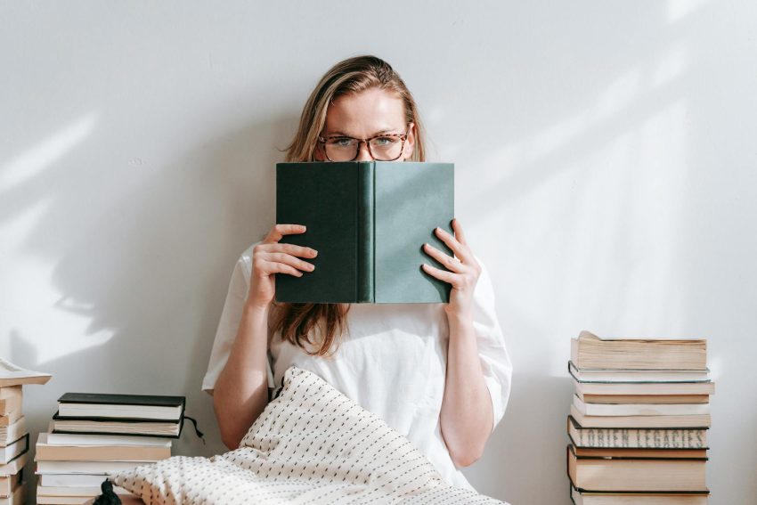 serious young woman sitting near stacks of books while doing homework assignment