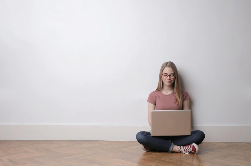 woman in pink crew neck top and jeans sitting down on the floor using laptop